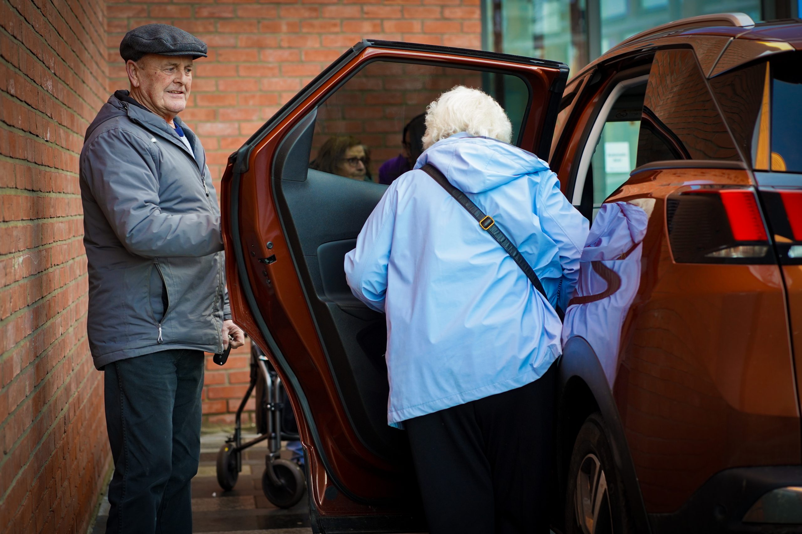 Volunteer driver holding a car door open for a service user