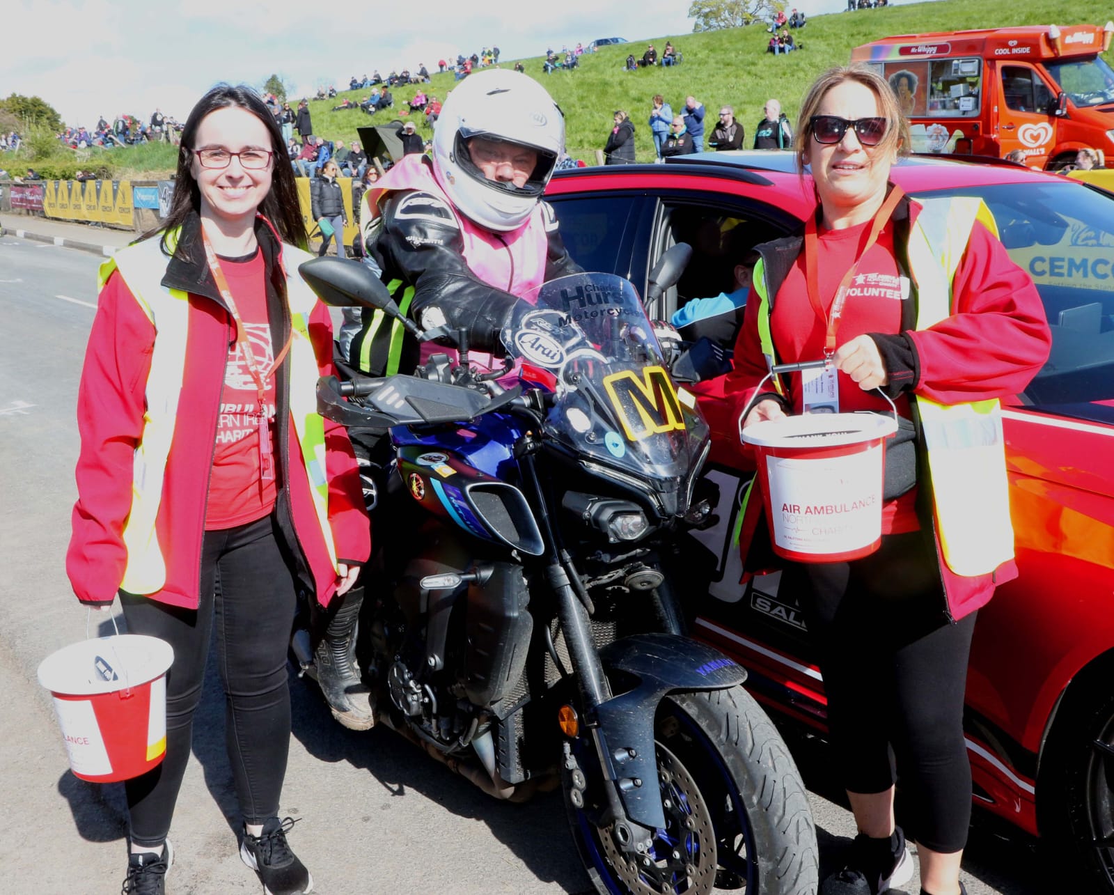 Photo of 2 Air Ambulance NI volunteers with their collection buckets, standing beside a motorcyclist
