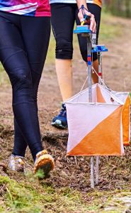 Some walkers approach an orienteering marker. You can't see their faces, only their legs.